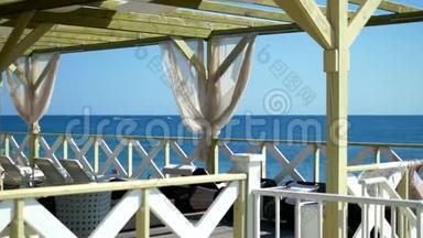 露台上有木制框架和白色窗帘以及海边沙滩上的躺椅.. 在夏天阳光明媚的日子。